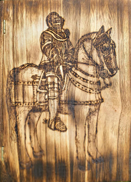 A wooden box shaped like a book, with a woodburned design of a knight on a horse.