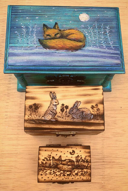 A set of differently sized wooden boxes, woodburned with various animal designs.