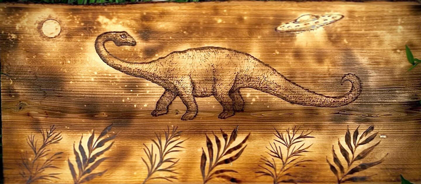 A woodburning of a dinosaur at night. A UFO is in the background.