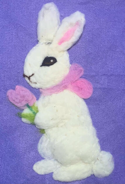 A felted bunny holding a tulip with a pink scarf.