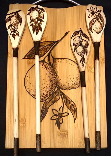 Four wooden spoons with a lemon design woodburned into them, on top of a cutting board with a lemon design.