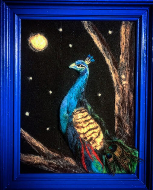 An image of a peacock made with colored wool on black felt. A real peacock feather is in the tail.