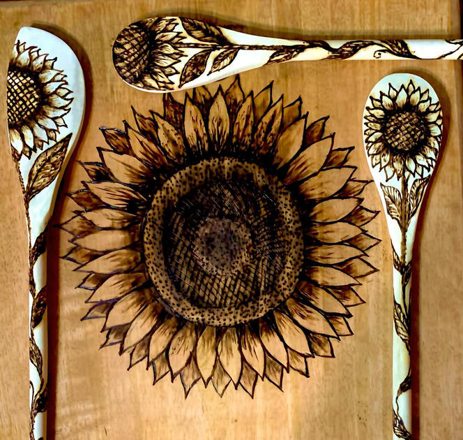 Three woodburned spoons with sunflower designs, placed around a cutting board with a large sunflower on it.